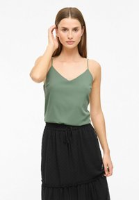 Groene cami-top met een V-hals, dunne bandjes en een gladde textuur, gecombineerd met een zwarte, gelaagde, gestructureerde rok met een trekkoord in de taille.