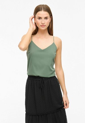 Camisetta verde con scollatura a V, spalline sottili e texture liscia abbinata a una gonna nera a strati, con un elastico in vita.