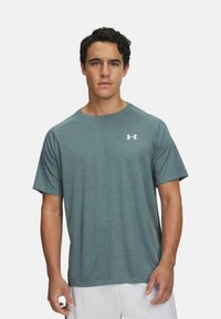 Camisa atlética de manga corta para hombre en tejido azul verdoso texturizado, con un cuello redondo y un pequeño logo blanco en el lado izquierdo del pecho.