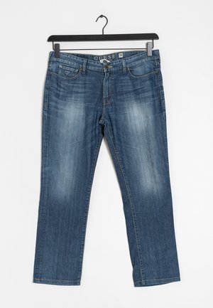 Niebieskie dżinsy z delikatnym wyblaknięciem na udach, z przodu guziki, szlufki na pasek, przednie i monety kieszenie, zawieszone na czarnym wieszaku.