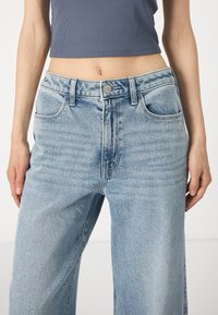 Απαλές μπλε τζιν παντελόνες σε φαρδιά γραμμή με ψηλή μέση, πέντε τσέπες και απαλή φθορά, συνδυασμένες με ένα κοντό ριγέ τοπ.