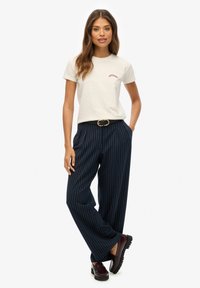 Jasnoszary bawełniany t-shirt z czerwonym logo, w połączeniu z granatowymi spodniami w paski o szerokich nogawkach i ciemnoczerwonymi butami z grubą podeszwą.