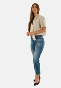 Camicia a righe con colletto e maniche corte con nodo davanti, abbinata a jeans aderenti blu chiaro e scarpe con tacco nere, mostrata di lato.