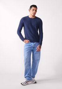 Marineblå strikkegenser med lange ermer, kombinert med lyseblå bukser med rette ben og grå joggesko, preget av subtile teksturer og enkelt design.