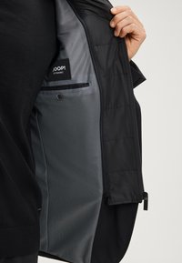 Czarna kurtka o gładkiej powierzchni i szarej, wzorzystej podszewce. Posiada metkę, kieszeń na guzik i zamek błyskawiczny u dołu.