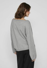 Grijze, oversized trui met een wijde halslijn en verlaagde schouders. Zacht gebreid materiaal en geribde mouwen. Gemaakt met zwarte broek.