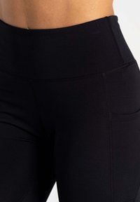 Schwarze Leggings aus einem glatten, dehnbaren Material, mit hohem Bund und einer Seitentasche. Enthält flache Nähte für Komfort und Langlebigkeit.