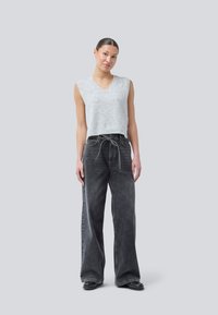 Ljusgrå ärmlös topp med v-ringning, ihop med vida mörkgrå denimjeans med knytmidja. Släta texturer och avslappnad design.