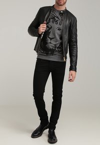 Veste aviateur en cuir noir, sweat-shirt gris avec un graphisme de lion, jeans noirs slim fit et chaussures noires vernies.