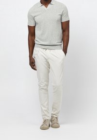 Polo gris clair à manches courtes, pantalon blanc ajusté et baskets beige. Tissu lisse avec une coupe cintrée et un détail subtil au niveau du col.