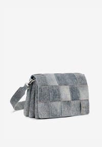 Szara torba na ramię w stylu patchwork, wykonana z denimu; ma prostokątny kształt, klapkę na zamek oraz odpinany pasek z metalowymi elementami.