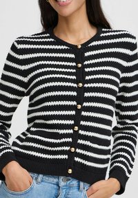 Cardigan rayé noir et blanc avec tricot texturé, doté d'un col rond, de manches longues et de boutons dorés sur le devant.