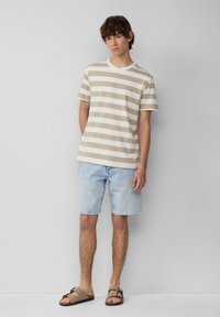 Gestreept katoenen T-shirt in beige en wit, gecombineerd met lichtblauwe denim shorts en bruine instapsandalen. Casual zomeroutfit.