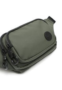 Borsa in tessuto verde scuro con texture, dotata di due scomparti con zip, cerniere nere e una toppa con logo circolare. Tracolla regolabile su un lato.