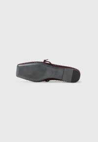 Chaussure plate avec un dessus en textile tissé bordeaux, semelle en caoutchouc noir et fond texturé. Dispose d'un petit nœud décoratif à l'avant.