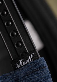 Black adjustable strap with round texture. Features a dark blue fabric accent with "Reell" embroidered in white. Simple and functional design.