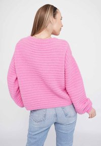 Rosa gestreifter Pullover mit lockerer Passform, Rundhalsausschnitt und gerippten Bündchen. Kombiniert mit hellblauen hochgeschnittenen Jeans.