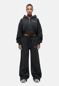 Czarna krótka bluza z kapturem i zamkiem błyskawicznym z przodu, w połączeniu z luźnymi czarnymi dresami z elastycznym pasem.