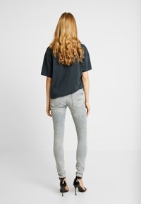 Camiseta oversized de color gris oscuro, jeans skinny de lavado claro con un ligero desvanecimiento, y tacones altos negros con tiras. Cabello largo y ondulado visible.