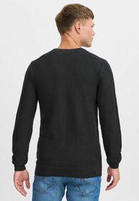 Svart teksturert genser med lange ermer og ribbede mansjetter. Har en rund hals og et vevd mønster. Brukes sammen med blå jeans.