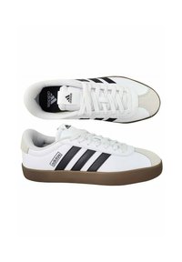 Biele športové topánky s hladkým zvrškom, obsahujúce tri čierne pruhy, okrúlu špičku a hnedú gumovú podrážku. Na dizajne sú texturované oblasti.