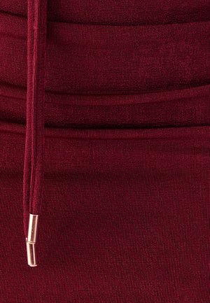 Bourgondische geribbelde stof met een elastische textuur, voorzien van een trekkoord met metallic accenten voor aanpassing en detail.