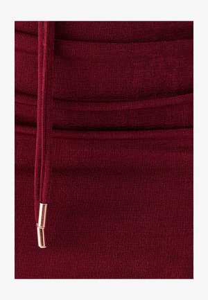 Bourgondische geribbelde stof met een elastische textuur, voorzien van een trekkoord met metallic accenten voor aanpassing en detail.