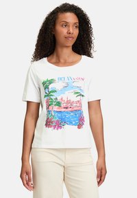 Hvid bomulds T-shirt med farverig grafik af palmer, blomster og en kystscene med teksten "OCEAN view". Korte ærmer, rund hals.