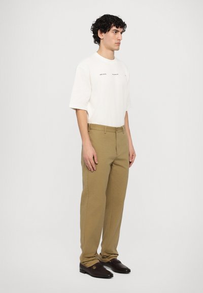 Beige chinos with a straight fit, paired with a loose-fitting white t-shirt featuring minimal black text. Black loafers complete the look.