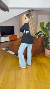 Zwarte blazer met triangulaire witte accenten op de achterkant, gecombineerd met lichtblauwe flare jeans en zilveren flats, weergegeven in een heldere binnenruimte.