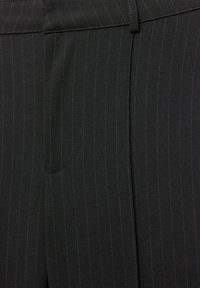 Crna tkanina s tankim vertikalnim prugama i tkanim remenom provučenim oko struka, dio krojenih hlača ili suknje.