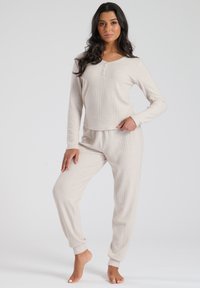 Top de manga larga beige de canalé con escote de tres botones y pantalones tapered a juego con puños elásticos. Tejido suave y texturizado.