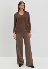 Brauner gestrickter Pullover mit V-Ausschnitt und Kragen, kombiniert mit braunen, weit geschnittenen Hosen. Weiche Textur, lockere Passform.