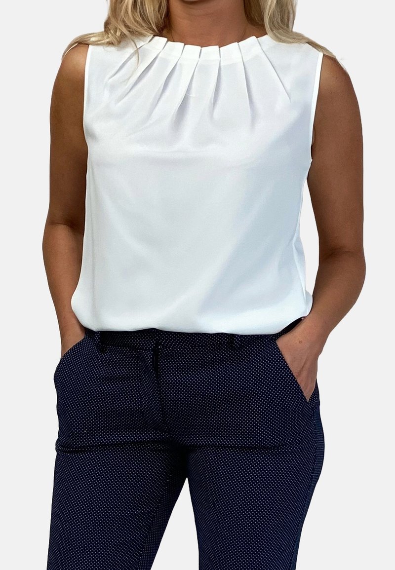 Vit ärmlös blus med plisserad design vid kragen. Matchad med marinblå byxor med prickar, som har sidofickor och en slät yta.