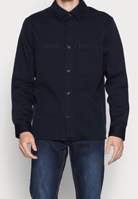 Chemise bleu marine à boutons en mélange de coton, avec col classique, deux poches poitrine et manches longues. Tissu texturé avec une finition lisse.