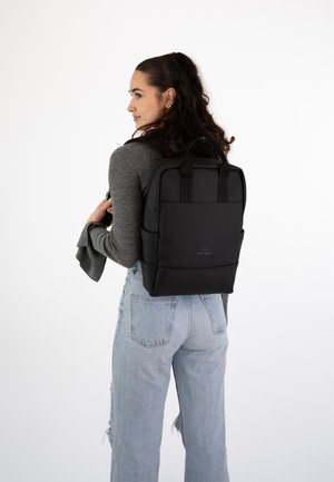 Rucsac negru cu curele de umăr căptușite, textură netedă și un design simplu. Dispune de buzunare frontale și un detaliu cu logo pe spate.