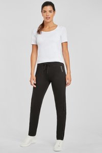 Schwarze Sweatpants mit Kordelzug, seitlichen Streifen und Logodetail. Kombiniert mit einem taillierten weißen T-Shirt mit kurzen Ärmeln und weißen Turnschuhen.
