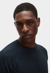 Námořnicky modrý pletený svetr s kulatým výstřihem a raglánovými rukávy, s jemnými texturálními detaily podél švů na ramenou.