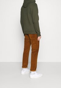 Olivgrön hoodie med snörning i huvan, tillsammans med bruna corduroybyxor med fickor. Vita sneakers och uppvikta ärmslut.