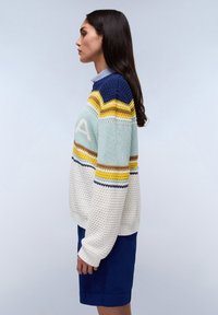 Gebreide trui met een mix van blauwe, gele en crèmekleurige strepen met textuurpatronen; gecombineerd met een blauwe rok.