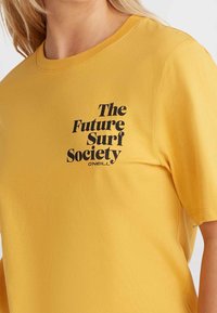 Camiseta de algodón amarilla con un diseño de texto en negro que dice "The Future Surf Society" y "ONEILL" en el pecho. Mangas cortas y cuello redondo.