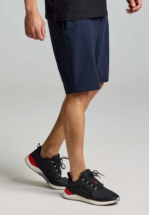 Shorts bleu marine en matériau léger, avec une coupe droite. Chaussures de sport noires avec des accents rouges et des détails en maille.