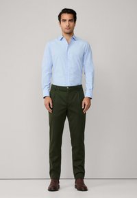 Camisa abotonada azul claro, pantalones oscuros verdes, botas marrones. Diseño ajustado con textura suave y aspecto entallado. Líneas simples y limpias.