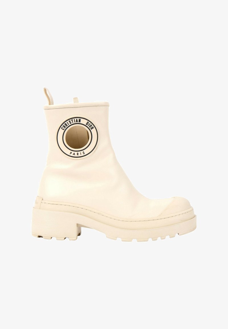 Bottine en cuir crème avec semelle épaisse, talon rond, languette de tirage et écusson rond noir et blanc du logo Christian Dior Paris près du haut.