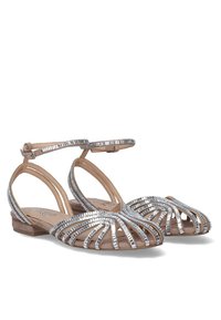 Sandalias planas plateadas con tiras, que presentan un diseño trenzado y una correa en el tobillo. El material texturizado contrasta con una plantilla suave de color marrón claro.