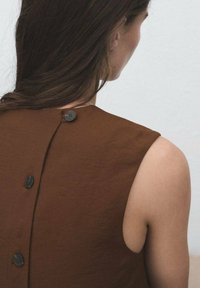 Bruine mouwloze top met een hoge halslijn en drie donkere knopen op de rug. Gladde textuur met een minimalistisch ontwerp.