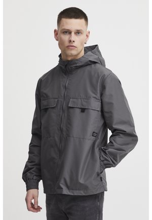 Veste grise à capuche avec fermeture éclair à l'avant, deux poches poitrine, poignets élastiques et finition texturée. Comprend une étiquette de la marque sur le côté inférieur.