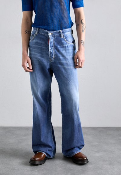 Hellblaue Denim-Jeans mit ausgestelltem Bein, ausgestattet mit einem Knopfverschluss und dezenten Verwaschungen. Kombiniert mit einem blauen Netzstrick-Top und braunen Stiefeln.