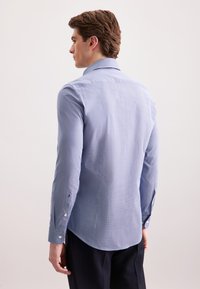 Camicia a maniche lunghe azzurro chiaro vista da dietro. Presenta un colletto aperto, tessuto testurizzato e polsini con bottoni e orlo arrotondato.