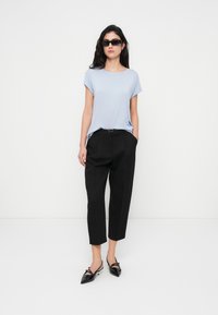 Ανοιχτό μπλε πουκάμισο με κοντά μανίκια, μαύρο παντελόνι σε στενή γραμμή και μυτερά μαύρα παπούτσια slingback. Απλός, καθαρός σχεδιασμός.